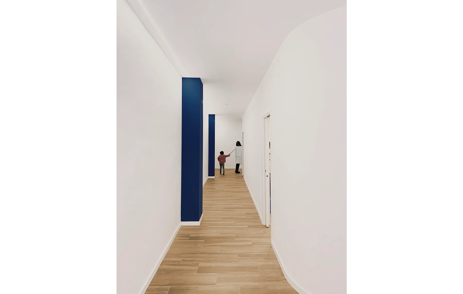 Pasillo moderno y luminoso de la clínica EPP con suelos de madera y detalles en azul, mostrando a una profesional acompañando a un niño.